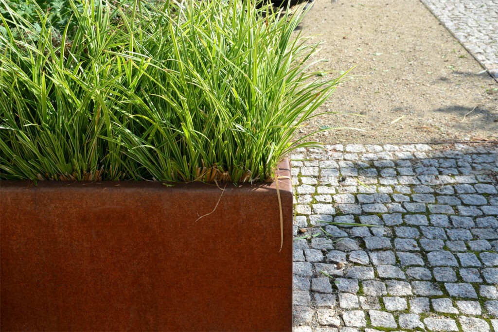 Blumenbeet wird von einem rostigen Blechdesign umrandet.